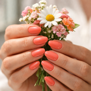 Summer nail colour in the UK in soft coral glossy manicure, photographed in natural sunlight